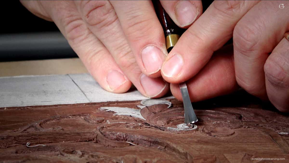 Fingers flat on dark wood, a small tool pinched close to its edge