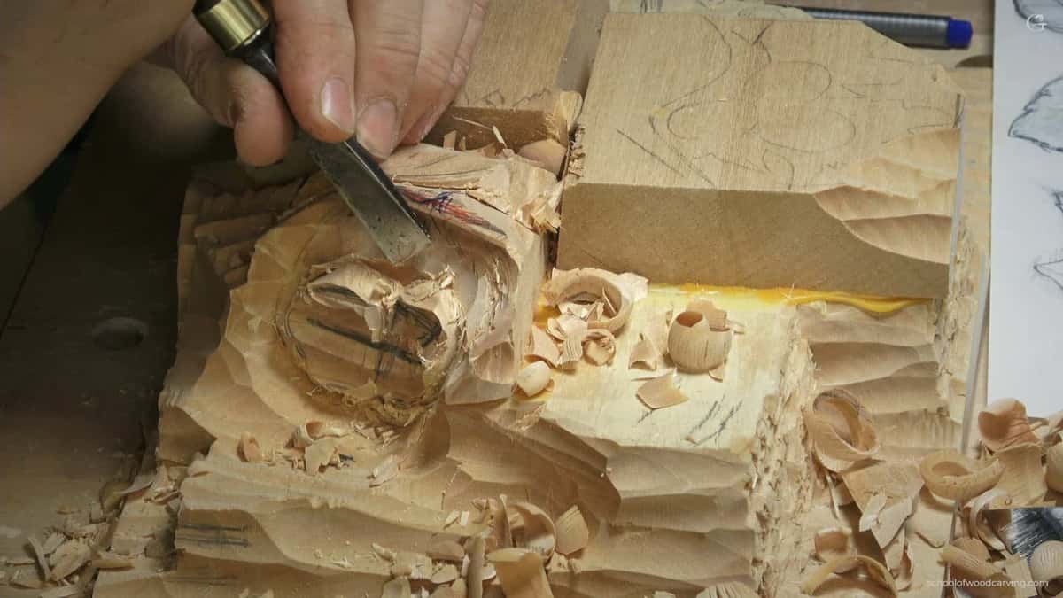 A plain plywood block takes the push while the chisel rounds one hazelnut, yellow clamp handle sitting just behind it
