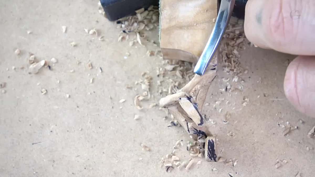 How small the work gets: a gouge shapes a stem no wider than a fingernail, chips like grains around it.