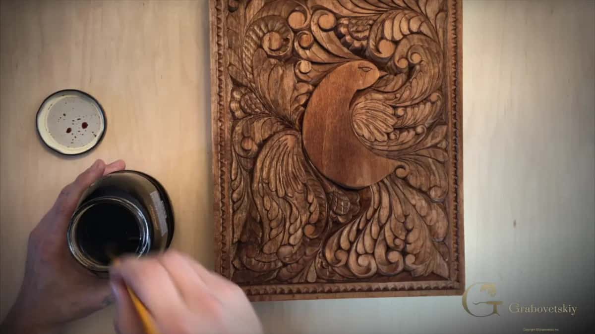 The bird panel now evenly brown all over, with a brush dipping into the open jar of dark finish.