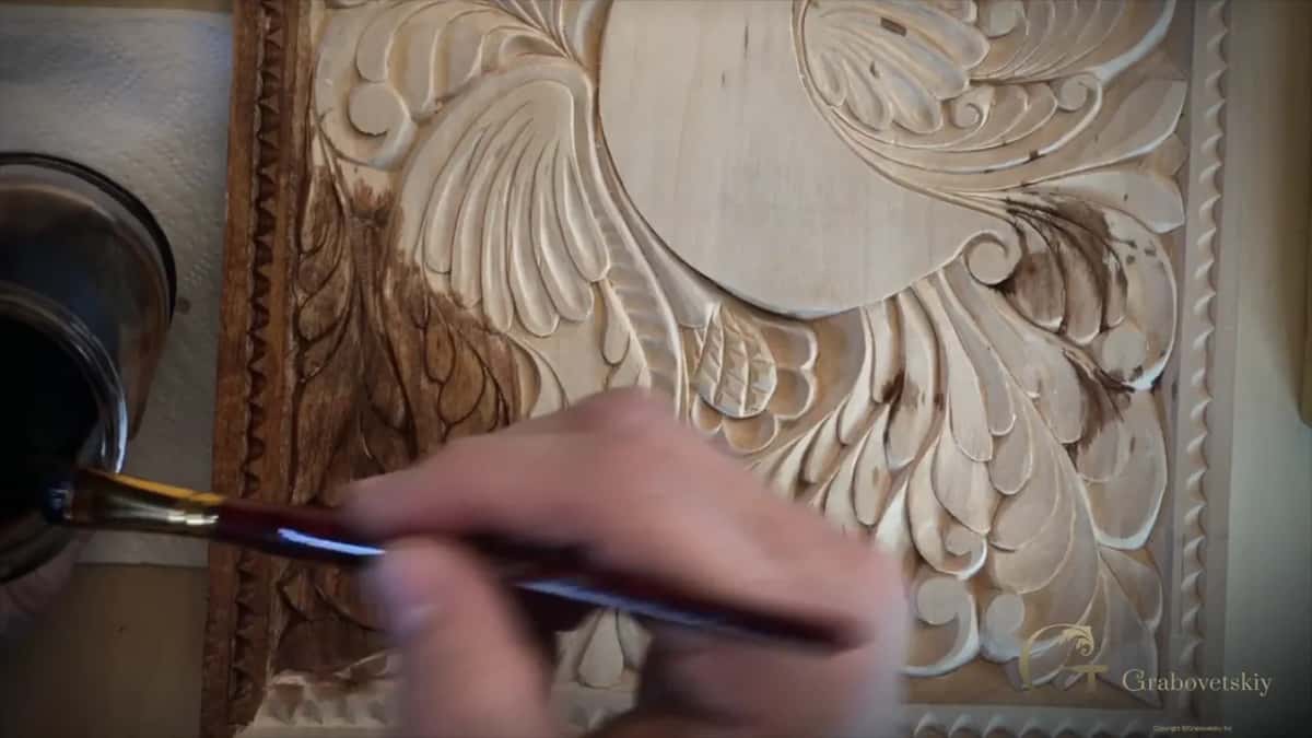A loaded brush comes in over pale carved wood, with the left edge of the panel already darkened.