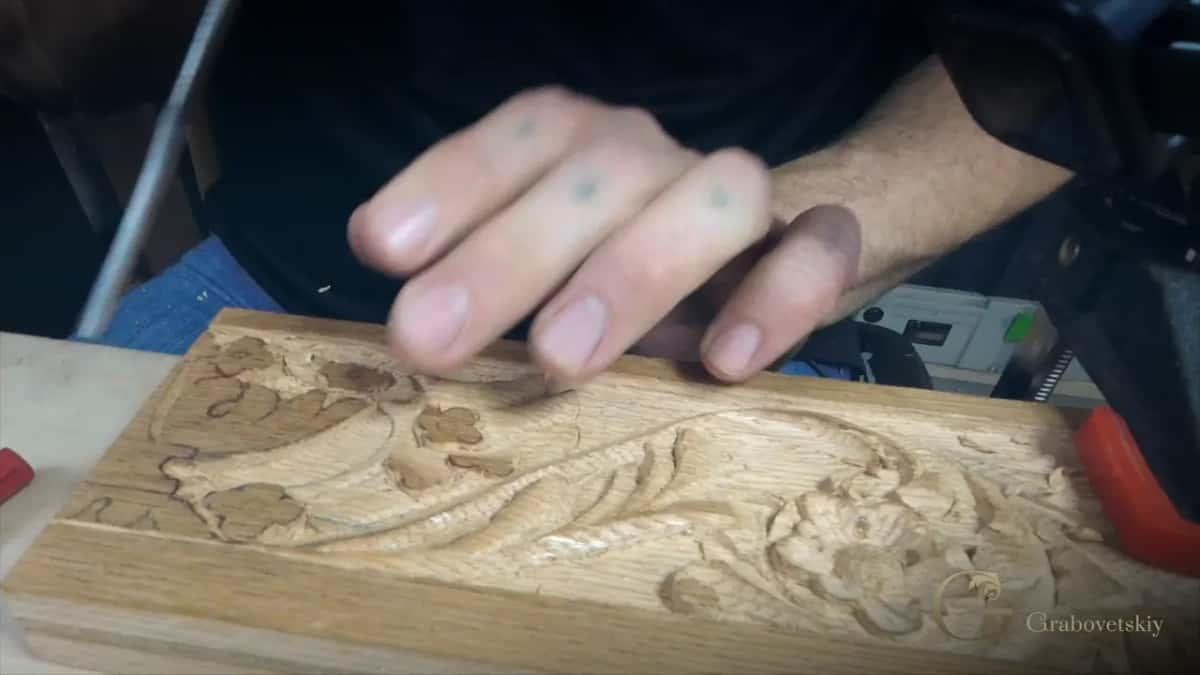 A carved rose and leaf relief sits clamped to the bench, a hand reaching toward it in a blur of motion.