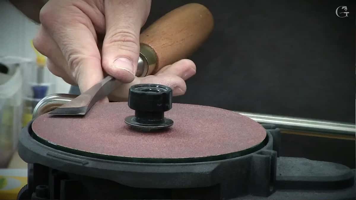 A small chisel with a brass ferrule held flat on a red abrasive disc.