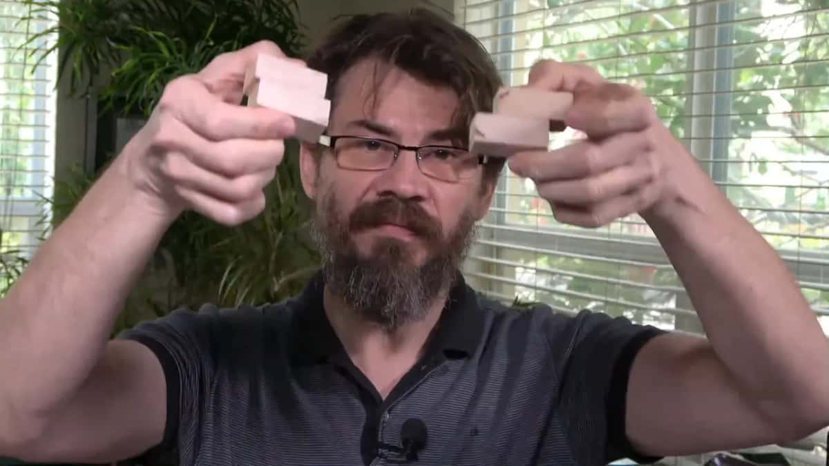 Two pale wood blocks are held up side by side near a bearded man's head for comparison.