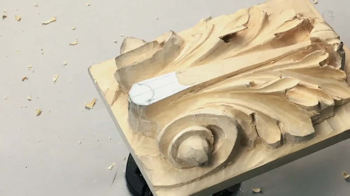 Deep leaves and a tight scroll come out of a pale block, with chips thrown across the grey table beside it.