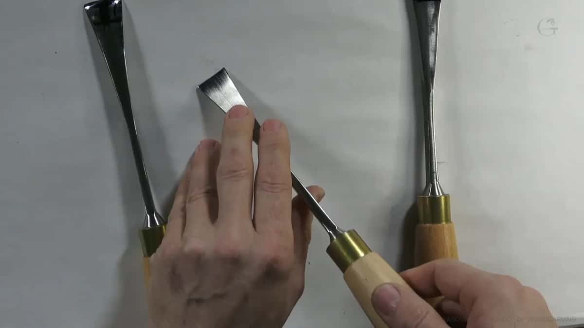 One tool is held up so the flat bevel behind its edge catches the light, two more lie on the white sheet.