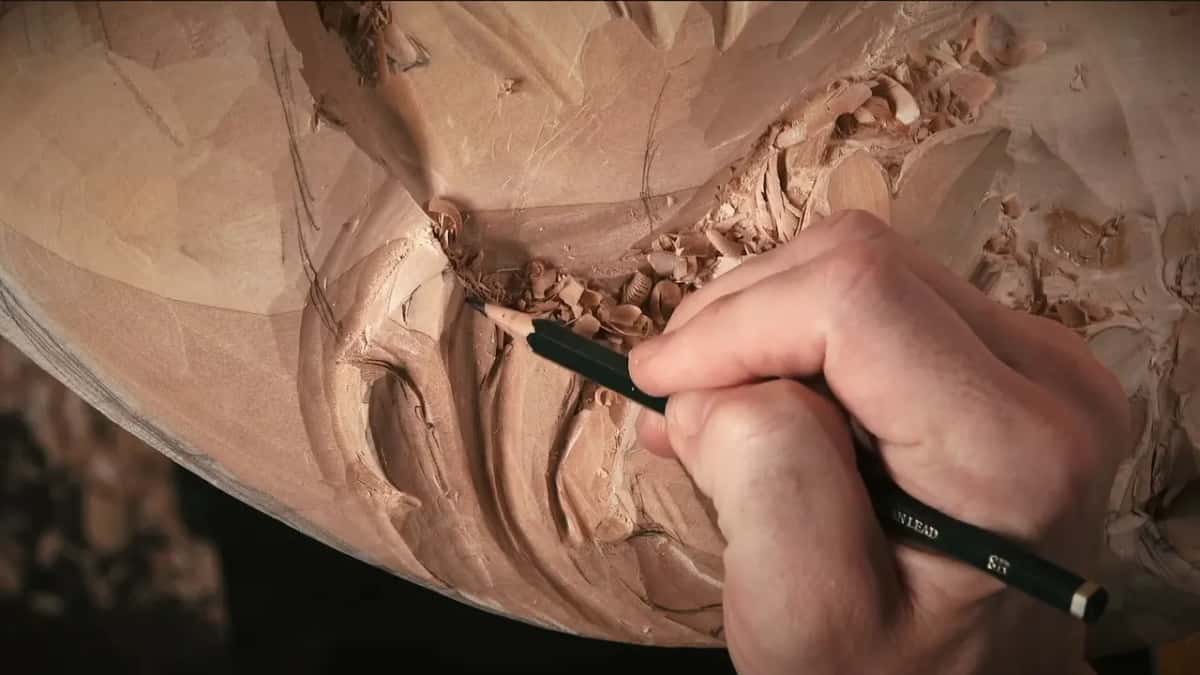 Pencil in hand, someone redraws a line on the reddish carving where the shape had been carved away.
