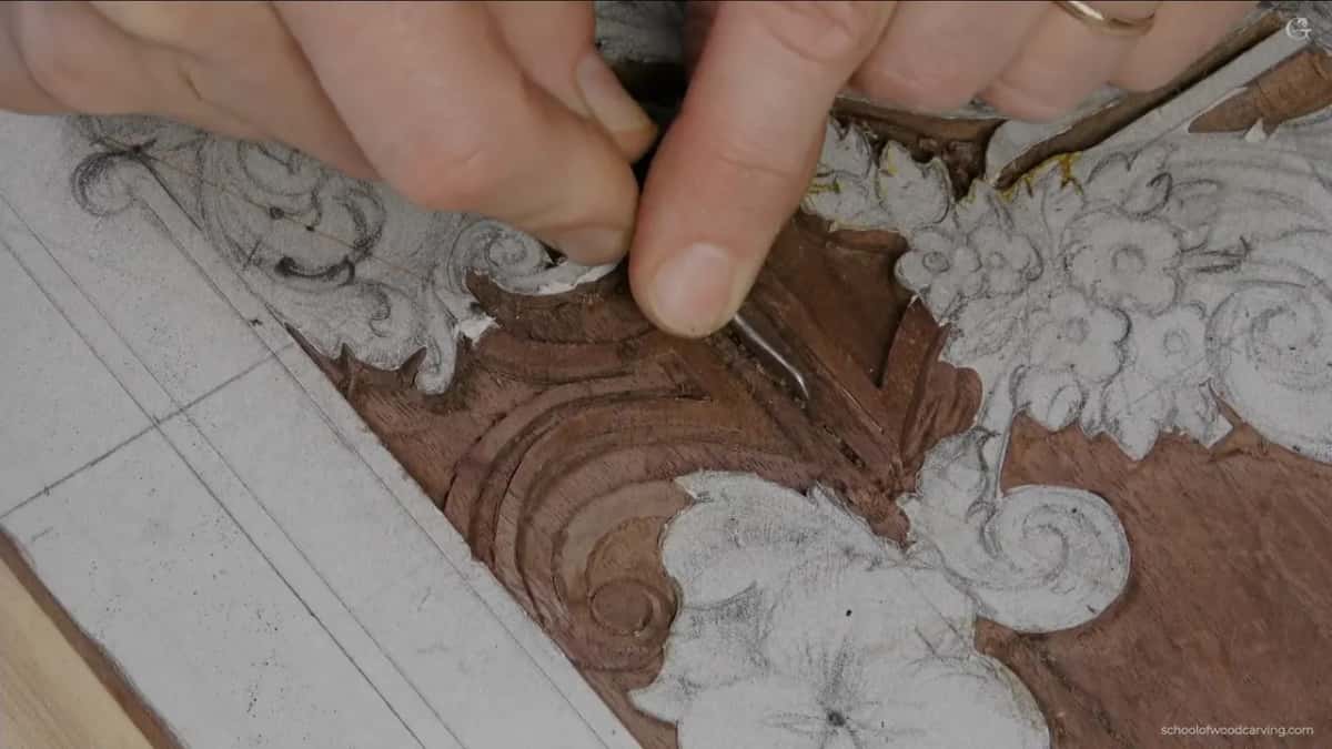 Yellow glue sits in a seam of a carved panel while a small tool picks at the edge of the chalked flowers.