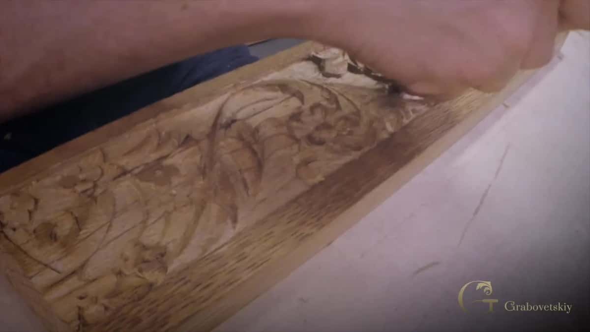 Leaves and flowers carved into warm oak, his forearm resting across the top of the carved band