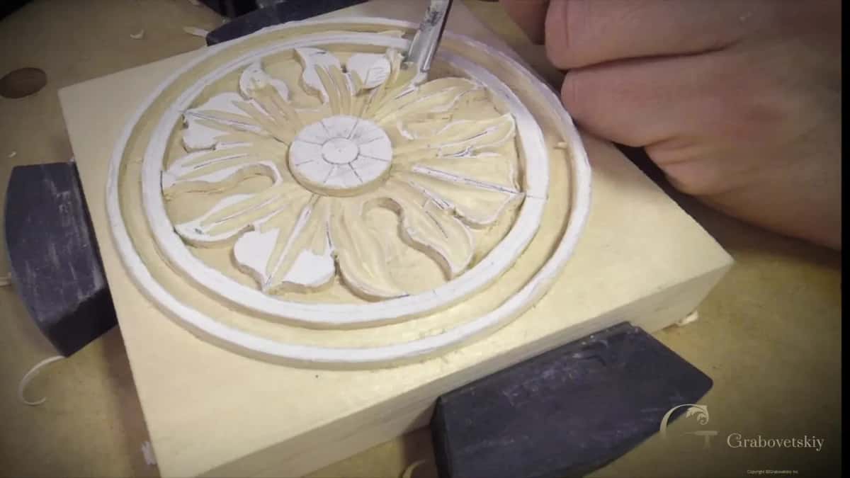 Carved rosette of shaped petals inside a turned ring, clamped between bench dogs with a small gouge above