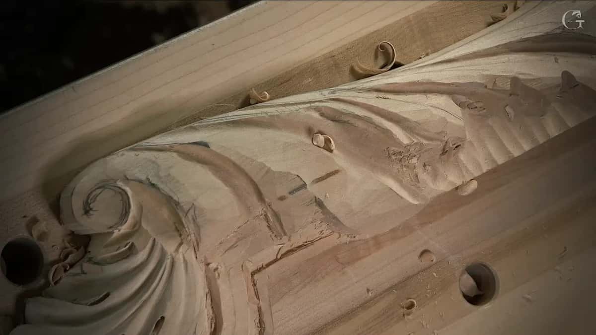 Loose shavings resting on a half-carved scroll, its layout lines still drawn across the ridges