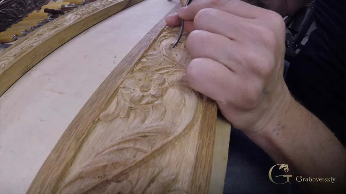Bent V-tool travelling along a curved oak rail where a flower and leaves are already carved