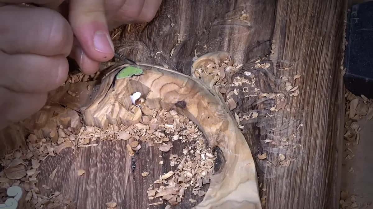 Dark swirling grain surrounds a small tool held against the wood, a green paint mark nearby.