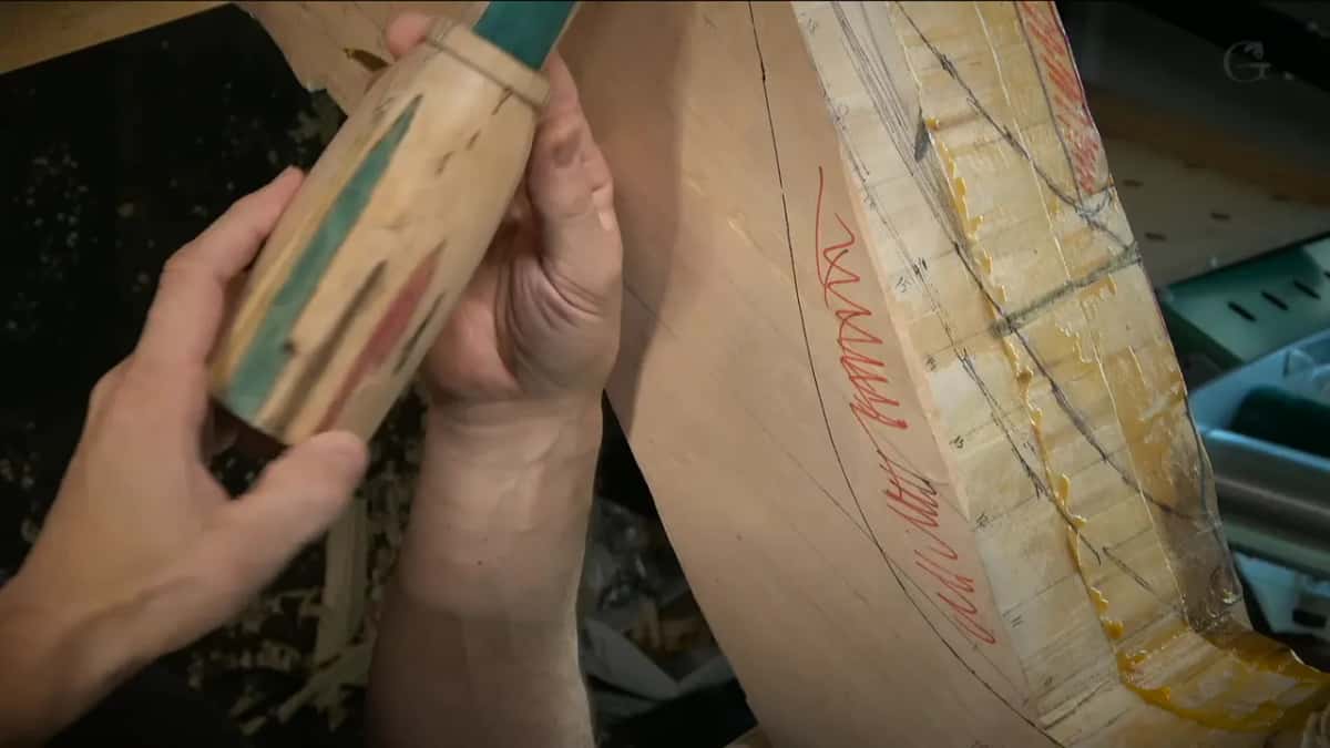 A curved panel glued from several boards carries red layout lines and wet glue along its seams.