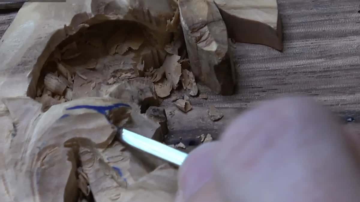 Fresh wood shavings curl inside a deep hollow as a gouge blade carves further into it.