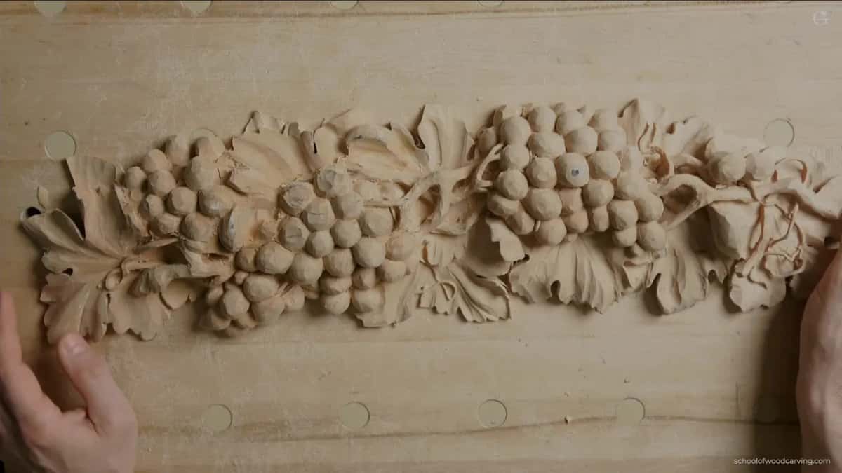 Grape cluster and leaf relief carving finished on a long wood panel.