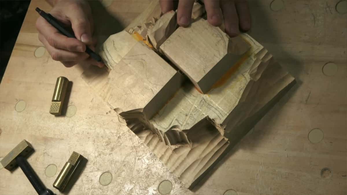 Pencil marking out a glued up relief block with brass bench dogs lying loose beside it