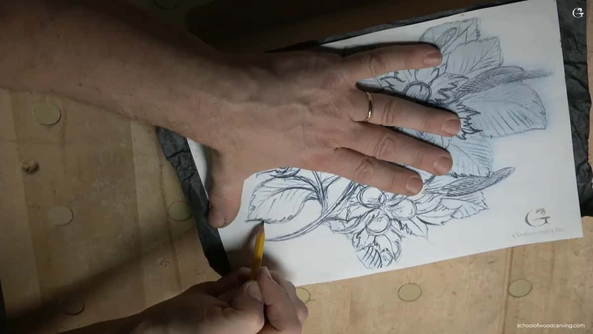One hand holding a printed hazelnut pattern down over dark carbon paper while the other traces the outline with a pencil