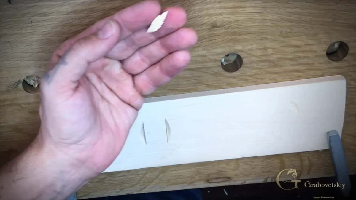An open palm holding one small basswood chip above the practice board it came out of, two notches left behind