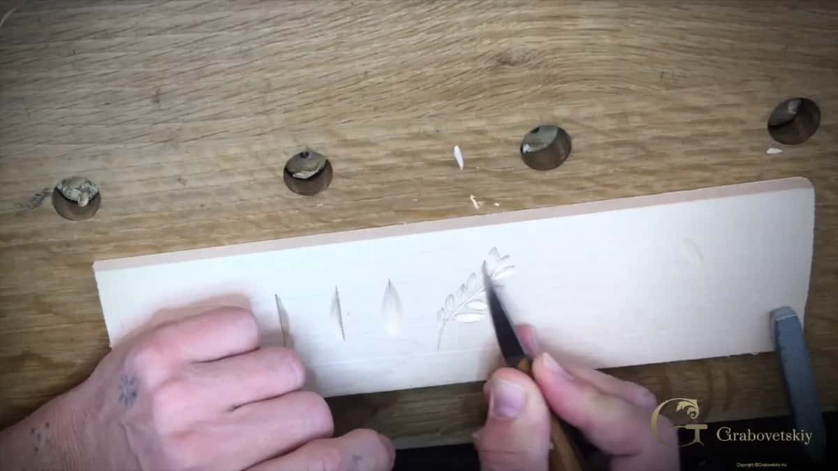 The penciled leaf spray now carved out of the basswood board, one loose chip on the bench, knife at the last leaf