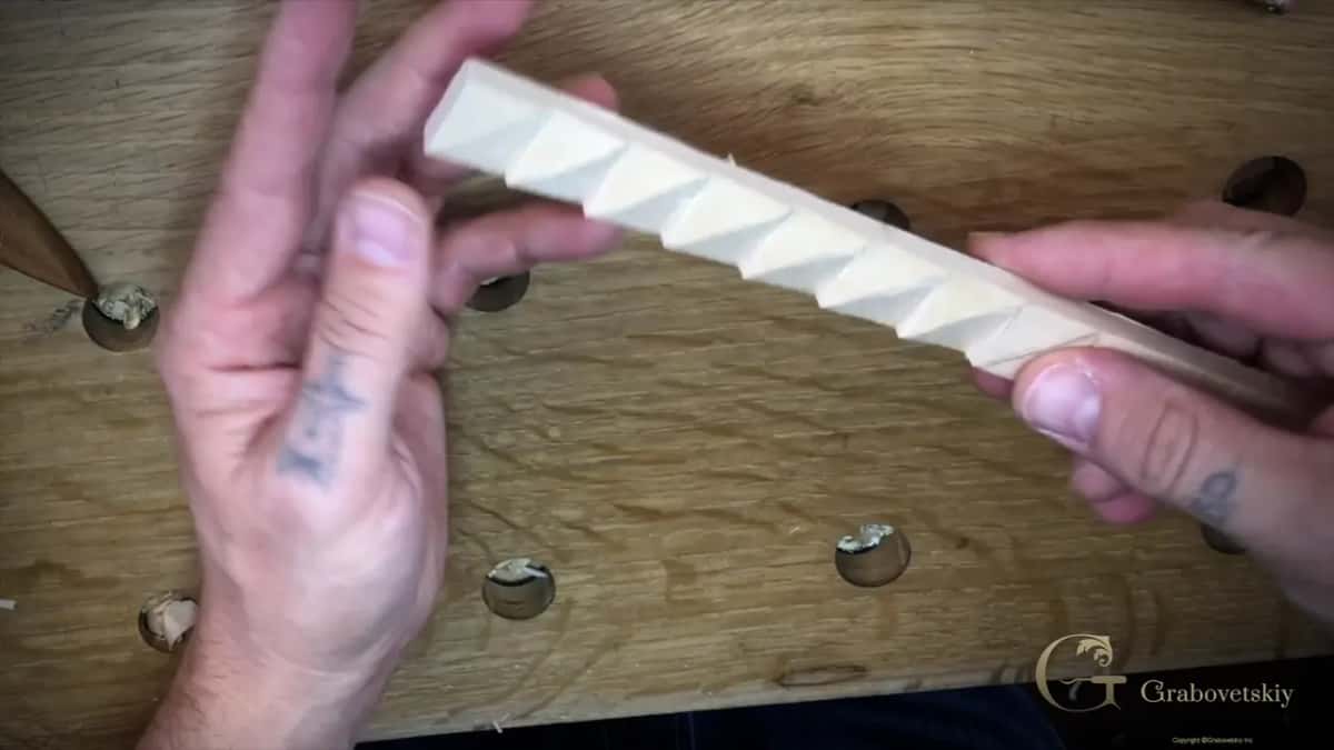 Two hands holding a finished basswood molding strip, a row of carved triangle facets catching light and shadow