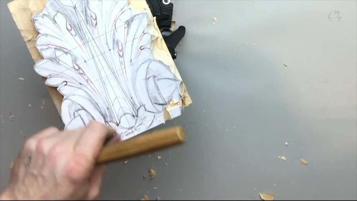 A paper acanthus drawing glued onto a basswood blank and clamped to the bench, shavings around it, gouge in hand