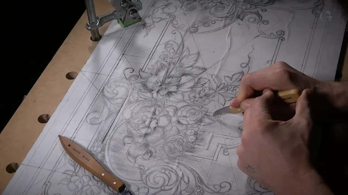 A full-size pencil pattern of a floral panel clamped to the bench, both hands guiding a small knife along one line