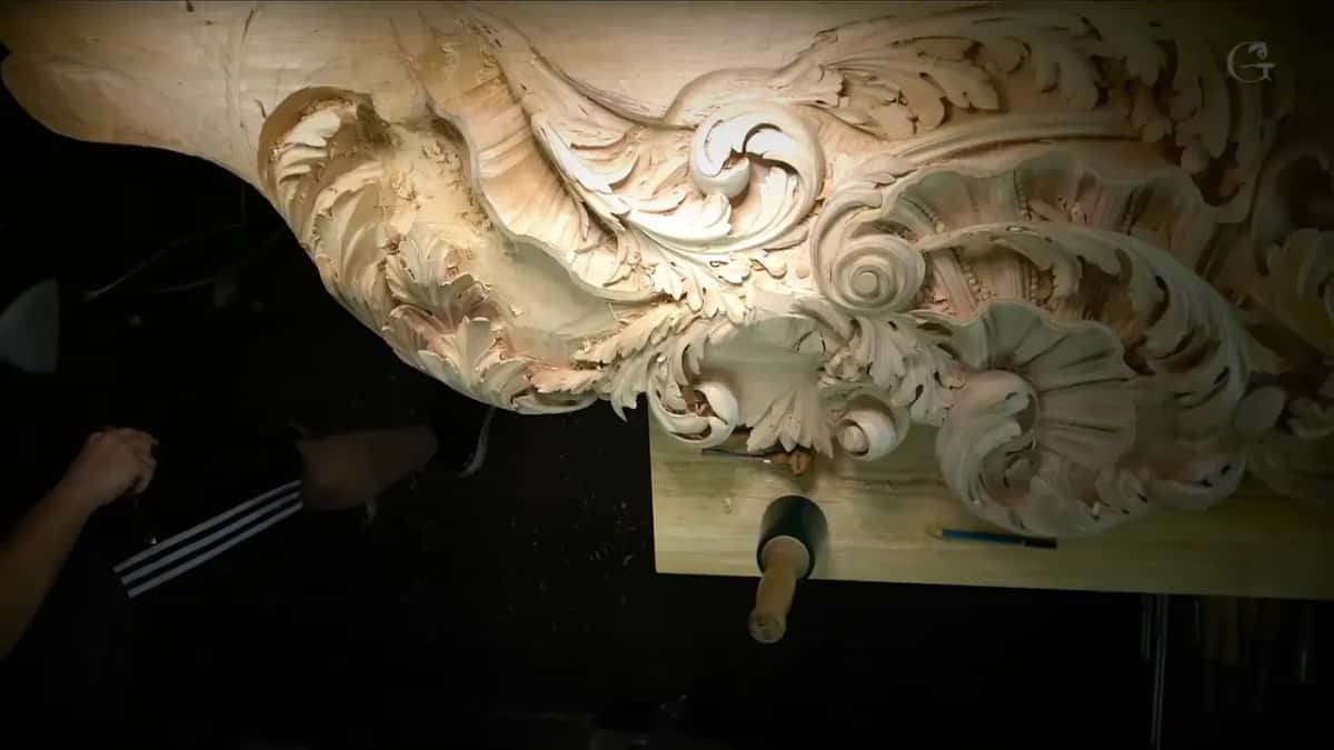 A deeply carved acanthus and volute frieze on the bench with a green rubber mallet, a gouge and a pencil beside it