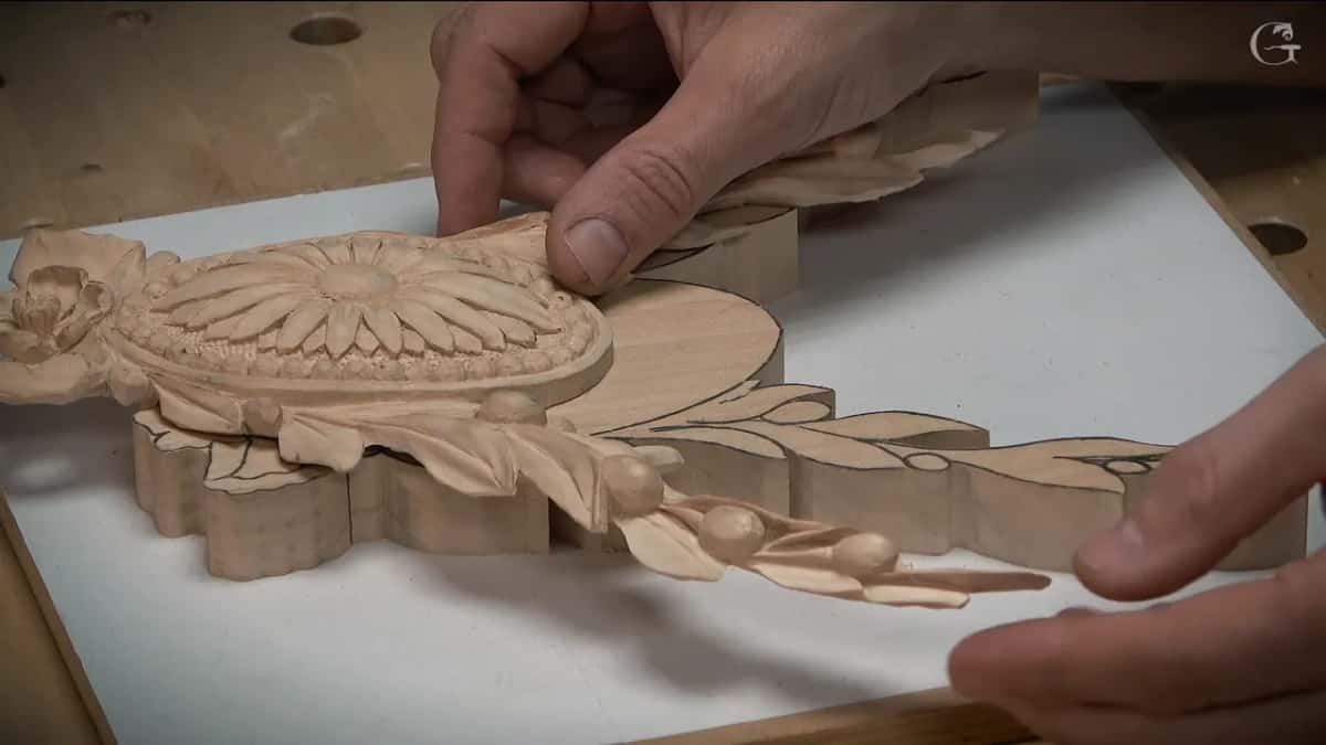 Close on the same piece: the daisy and leaves finished at one end, the other end still flat wood under pencil lines.