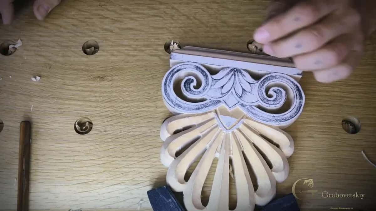 A small palmette piece half carved and half still in pencil, on an oak bench with a mallet handle at the left.