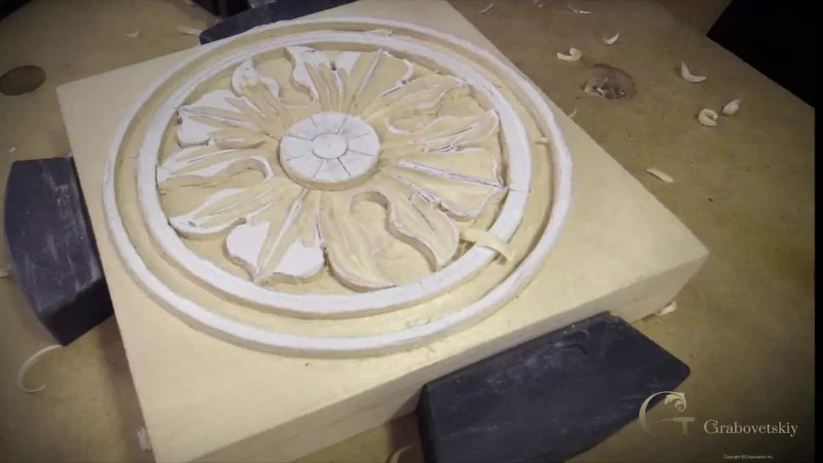 A carved flower rosette sits finished on its square blank, side light picking out every petal.
