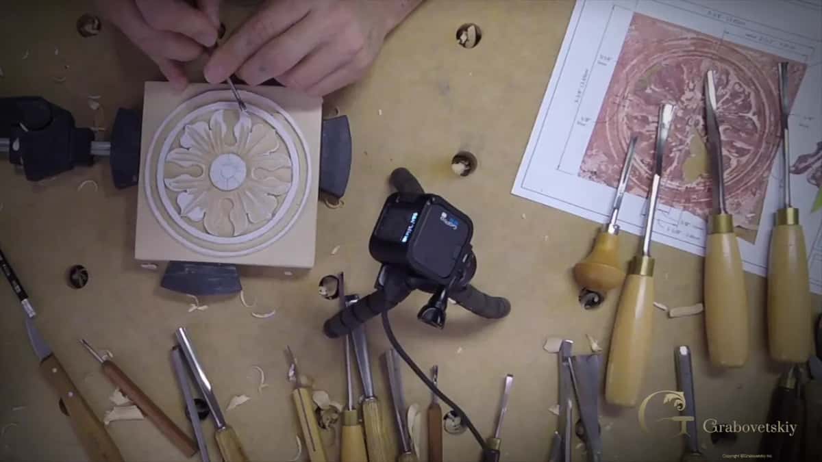 Overhead view of the bench with the rosette clamped down, rows of chisels and a printed reference photo.