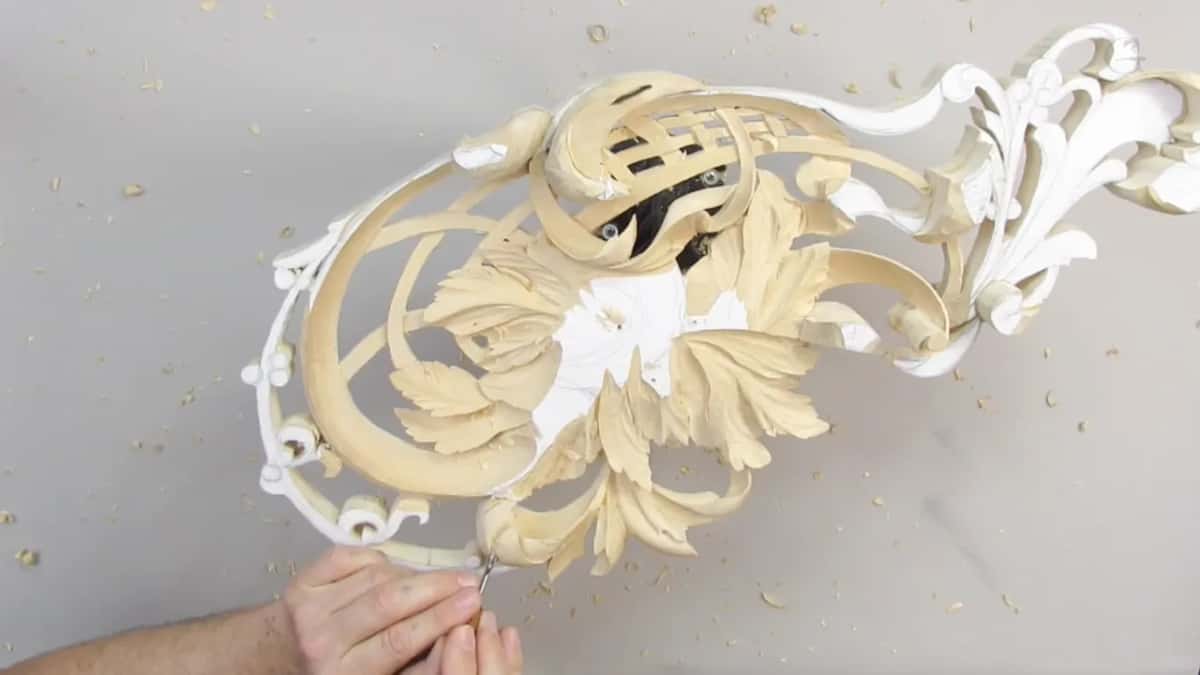 Painted white sections sit beside freshly carved pale wood, with hands steadying the ornament.