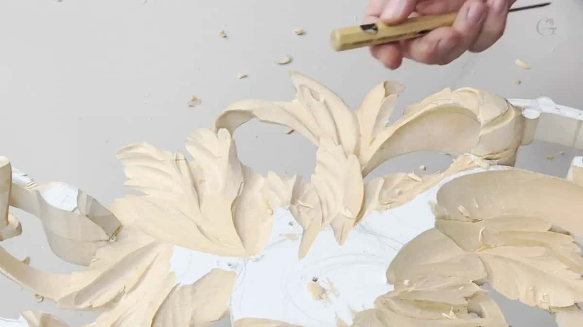 Fresh carved leaves curl above a white painted core while a small gouge waits over the work.