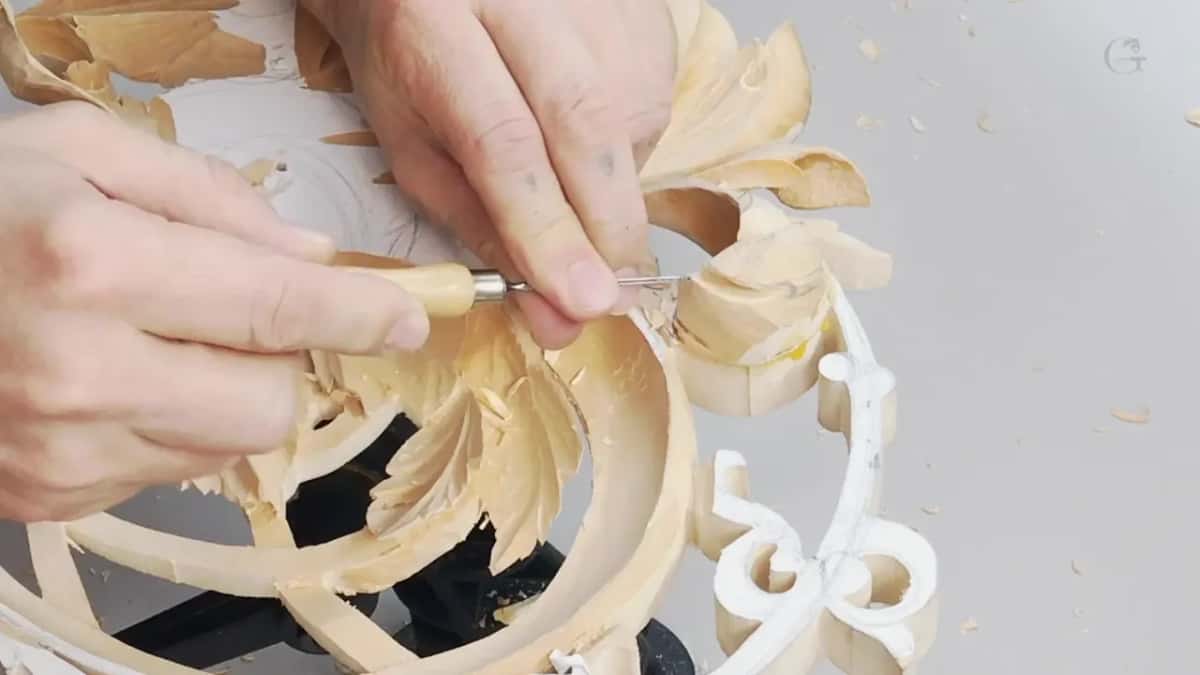 Working with both hands, a carver steers a gouge along the edge of the openwork.