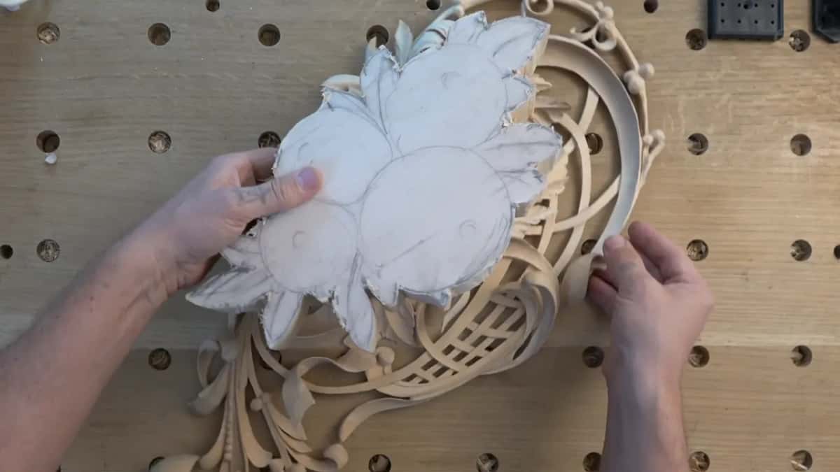 Hands hold a roughed white blank over a finished lattice carving to see how the two line up.
