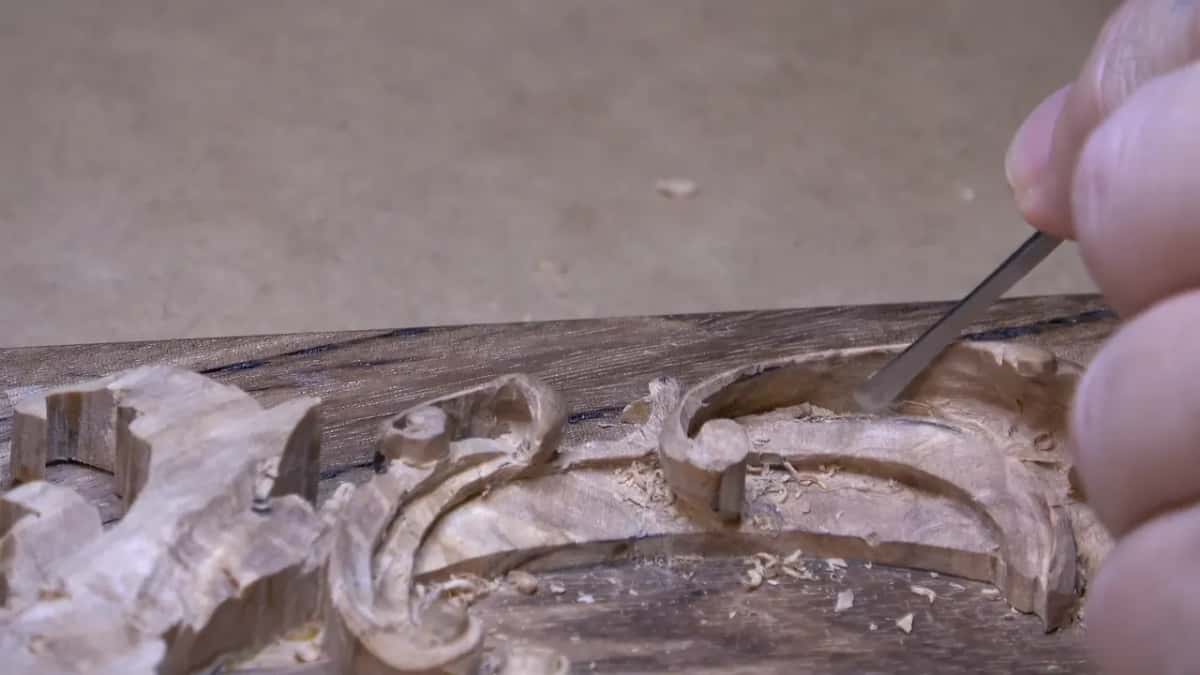 Shavings catch in the eroded grain as a narrow blade shapes a scroll into that same grey board.