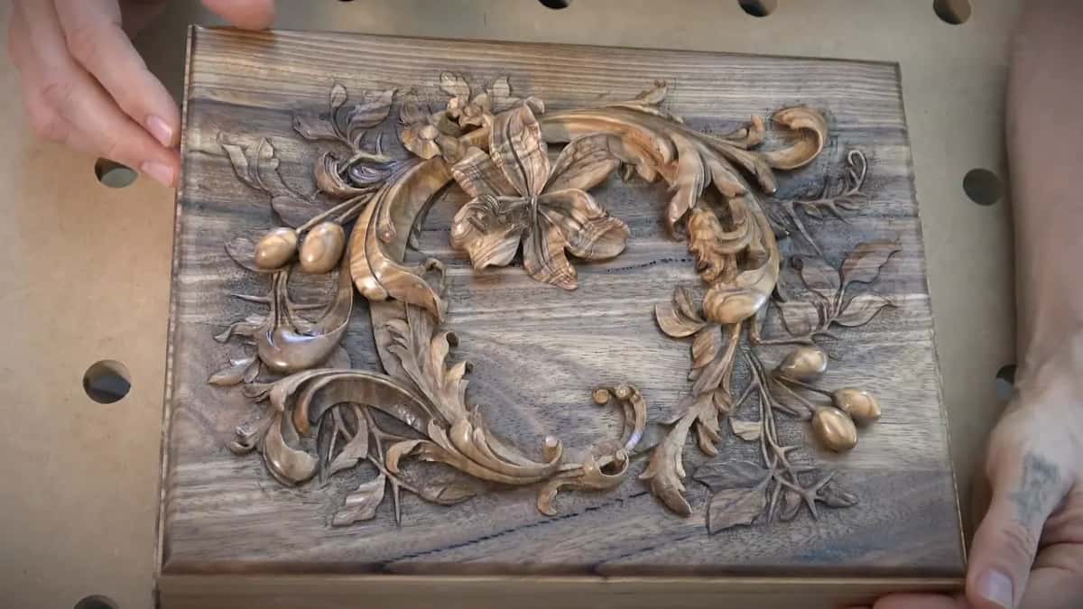 Two hands rest at the edges of that panel while light slides off the smooth carved petals.