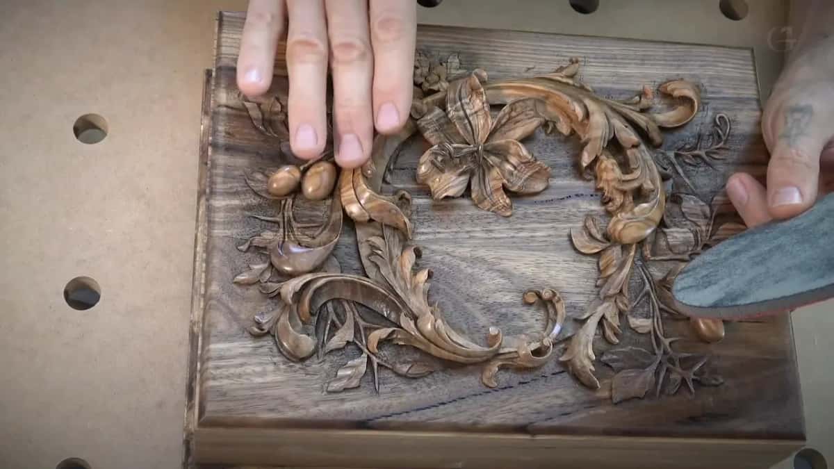 An abrasive pad rides along the border of the finished panel, one hand flat on the carving.