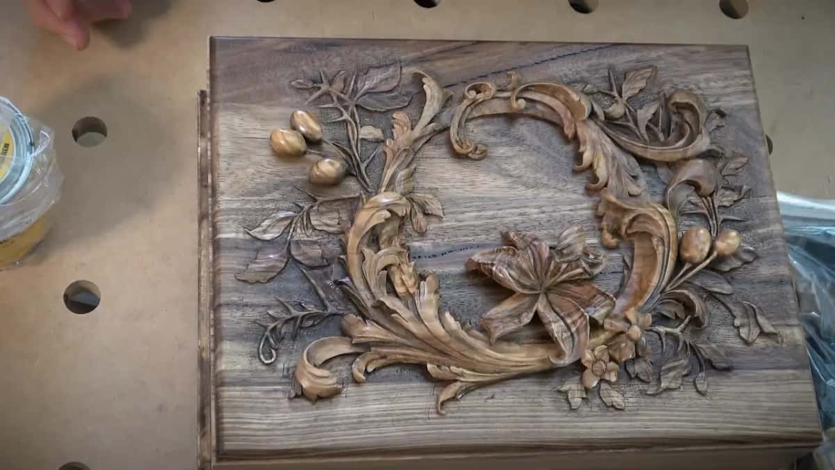 The carved panel sits inside its frame on the bench, seen from the far end beside a small jar.