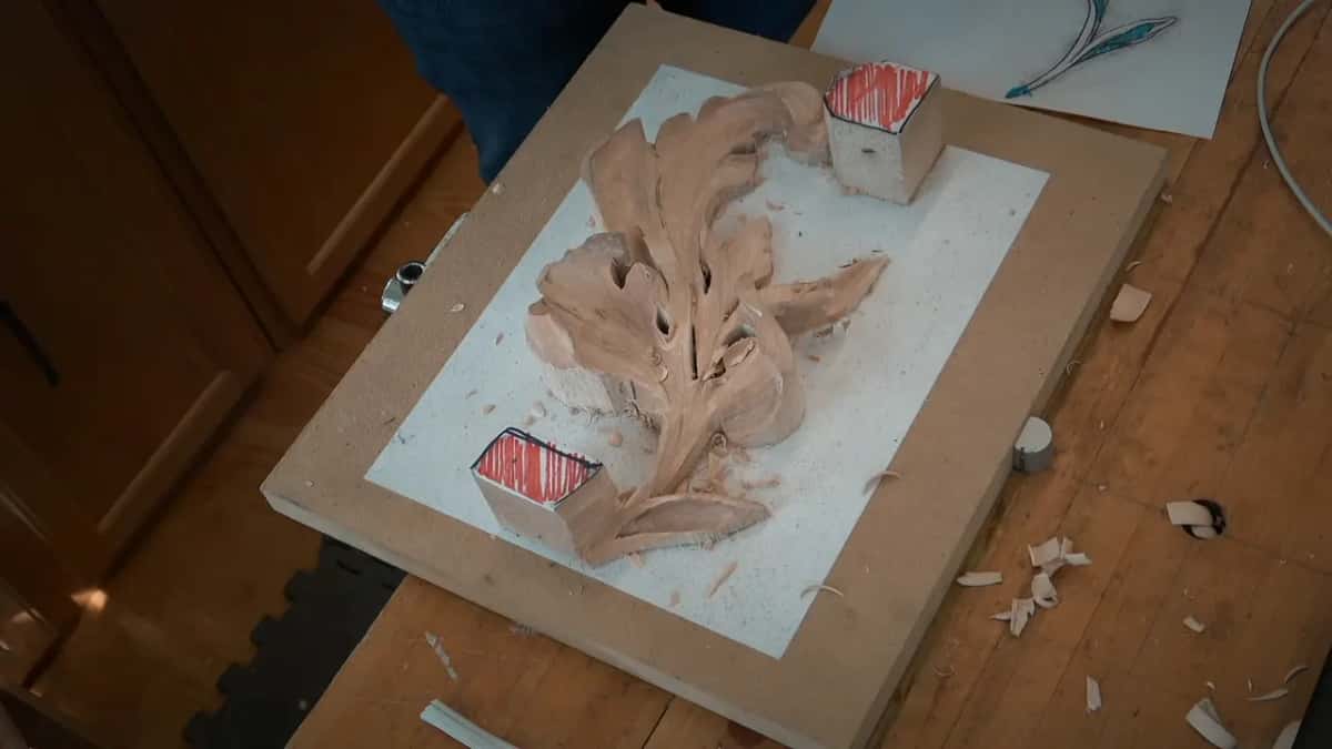 Roughed out of solid wood, a leaf shape rises off a white board with shavings scattered around.