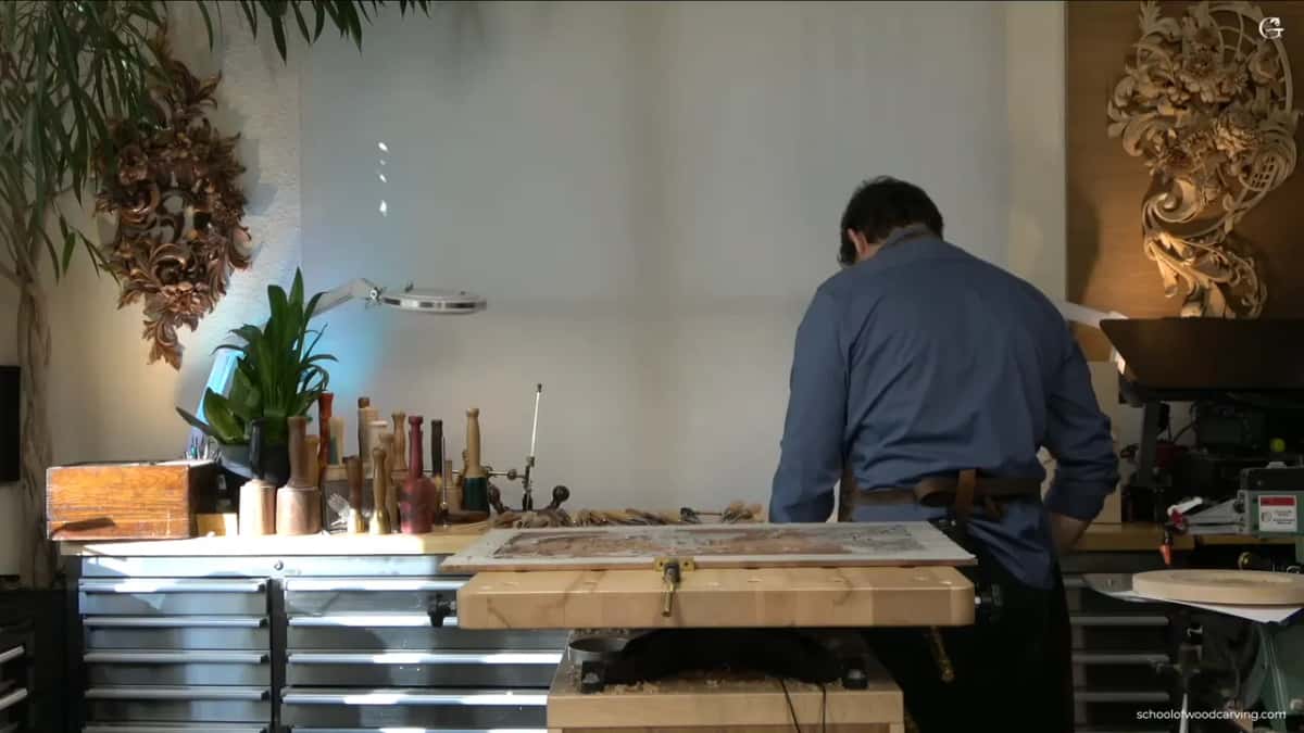 Finished panels hang on both shop walls while the carver works at a lit bench between them.