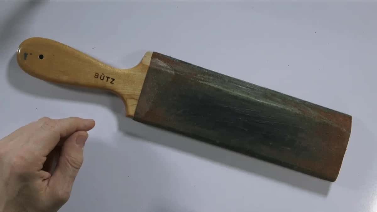 A big paddle strop with a maple handle, its leather face stained dark green from years of compound.