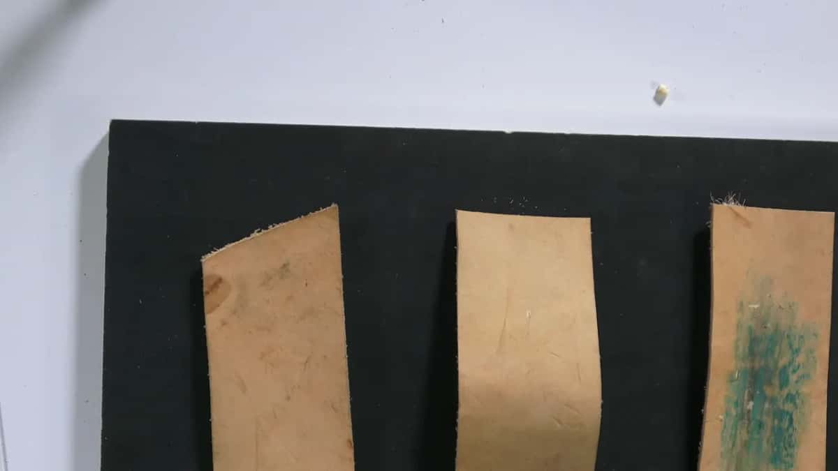 Three leather strips glued down on a black board, and the right hand one is already rubbed green with compound.