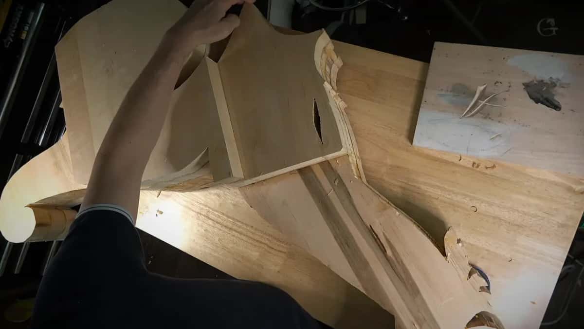 An arm lifts a carved wood scroll piece with an open section through its center, a stained rag resting nearby.