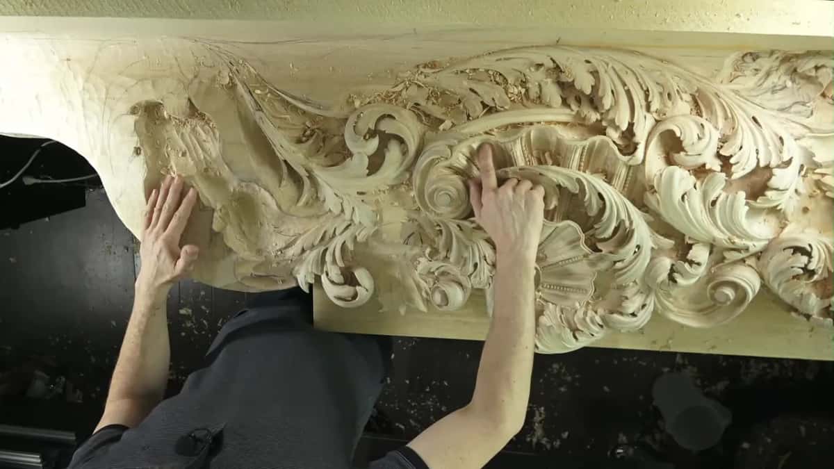 Reaching up into a large carved leaf and scroll panel overhead, hands press a section still plain.