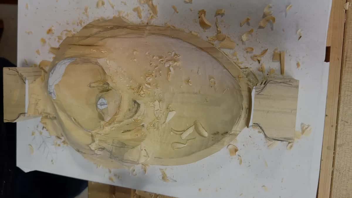 Wood shavings surround a rough, oval shaped carving blank still marked with pencil guidelines.