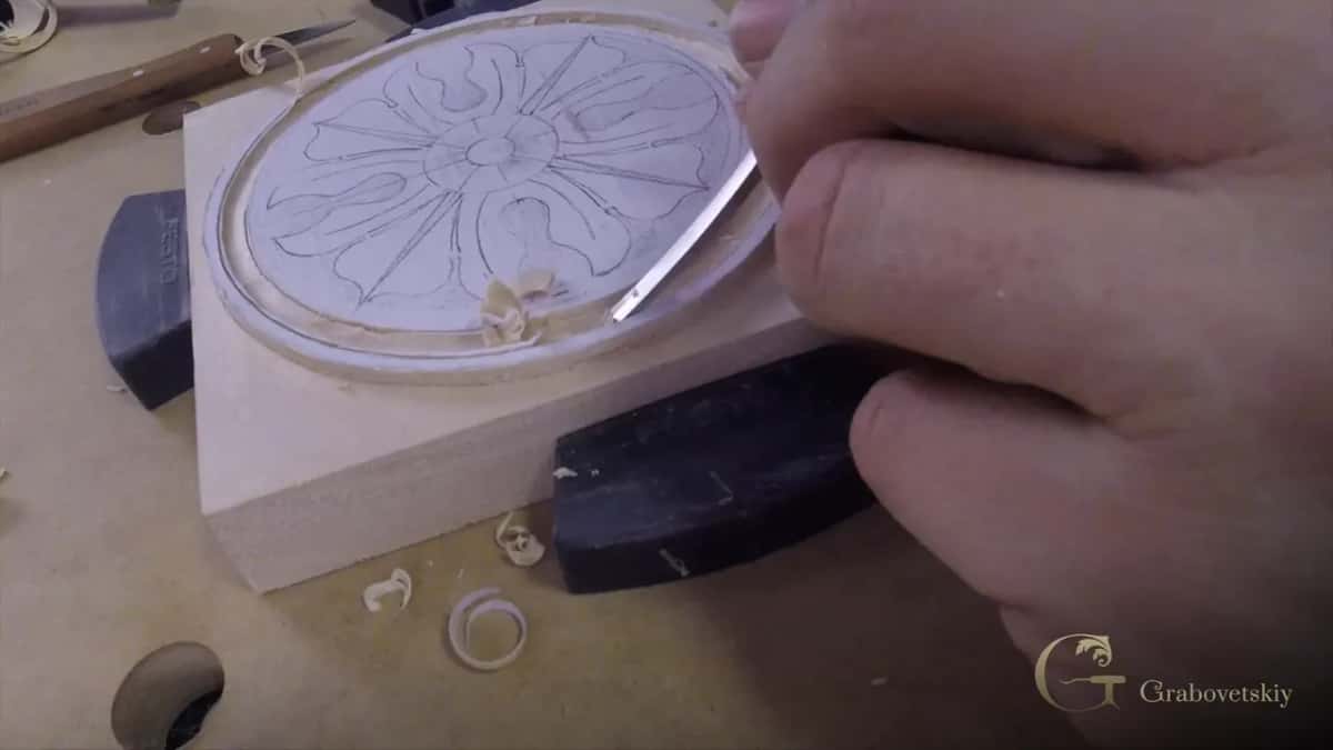 A round floral rosette takes shape under a narrow blade, its pencil guide lines still visible in the uncarved center.