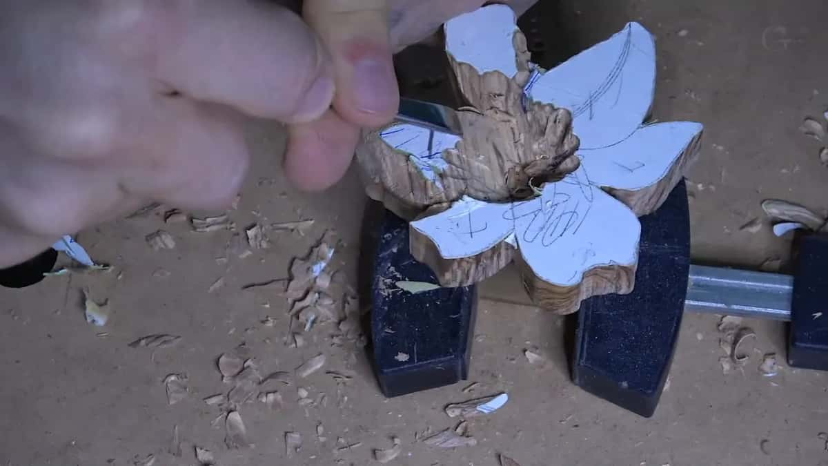A gouge works at the center of a flower blank whose petals are still covered by the white paper pattern.