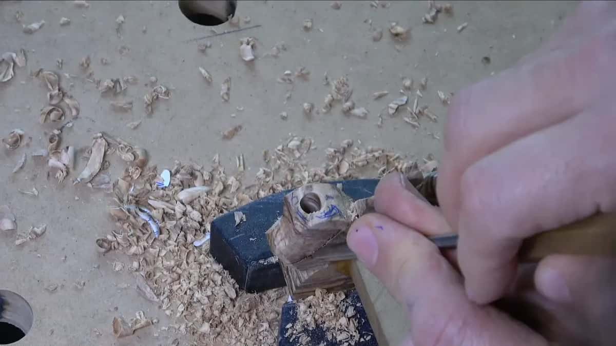 Clamped in a bench vise, a wood piece with a drilled hole is held while a tool works on it.